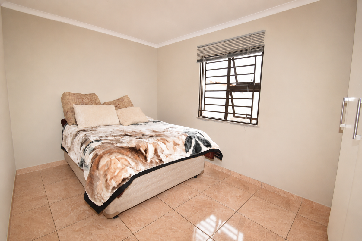 A functional bedroom featuring tiled flooring, a window with security bars and venetian blinds, and a built-in wardrobe.