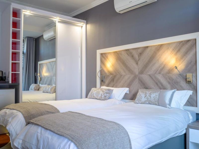 Modern bedroom featuring a custom wood-paneled headboard, integrated lighting, mirrored built-in wardrobes, and a wall-mounted air conditioning unit.