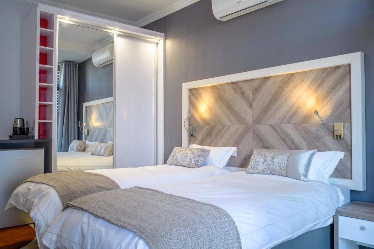 Modern bedroom featuring a custom wood-paneled headboard, integrated lighting, mirrored built-in wardrobes, and a wall-mounted air conditioning unit.
