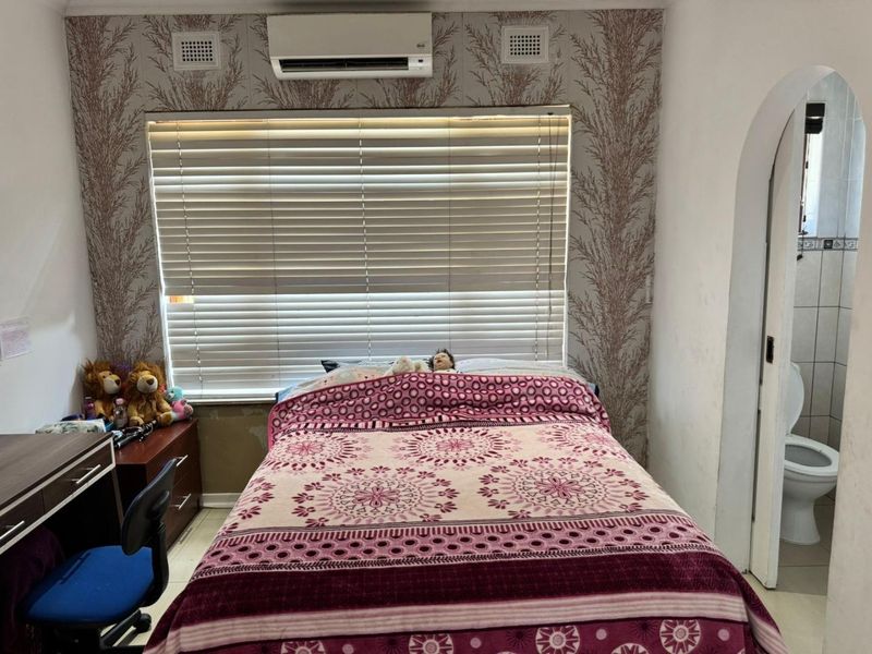 Bedroom featuring a split-system air conditioner, venetian blinds, and an arched doorway leading to an adjacent bathroom.