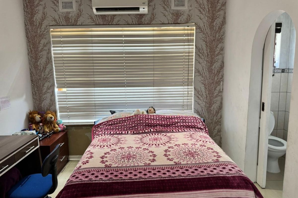 Bedroom featuring a split-system air conditioner, venetian blinds, and an arched doorway leading to an adjacent bathroom.