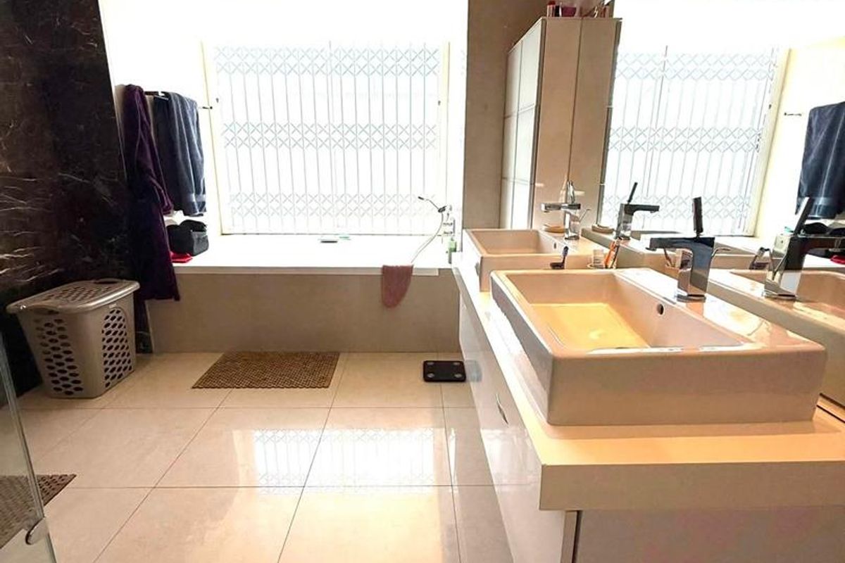 Modern bathroom featuring a double vanity, large wall mirror, built-in bathtub, and polished porcelain floor tiles with recessed ceiling lighting.