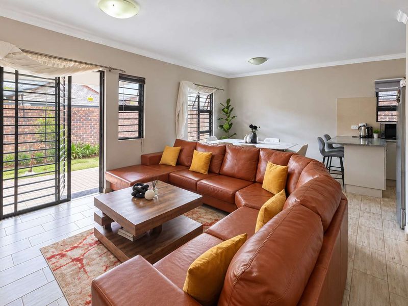 Open-plan living and dining area featuring tiled floors, neutral walls, and direct access to the rear patio through a security gate.