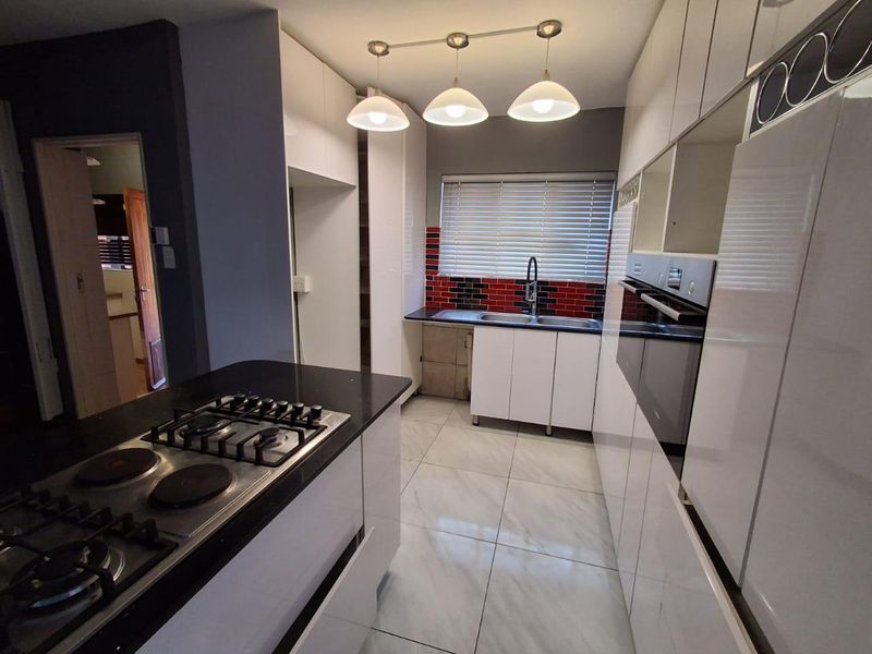 Modern kitchen featuring white high-gloss cabinetry, black countertops, a gas and electric hob, built-in oven, and tiled flooring with a red and black tiled backsplash.