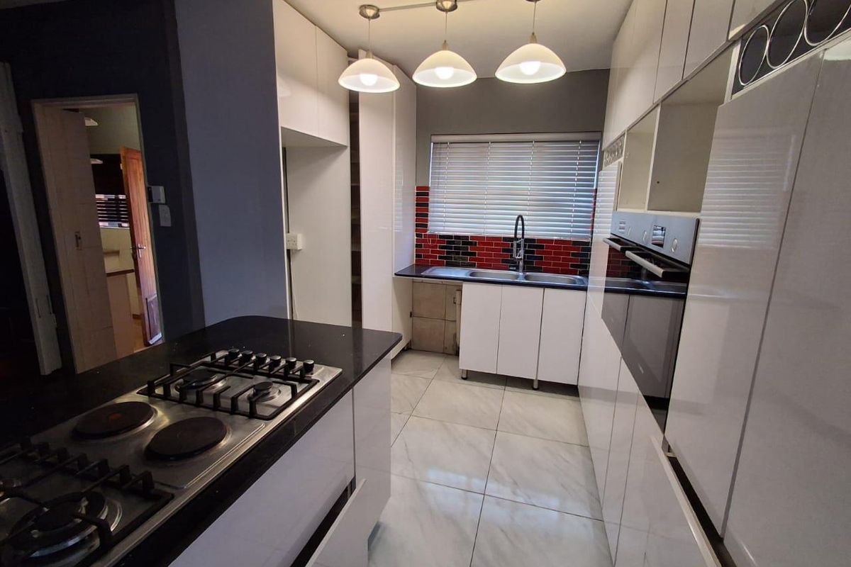 Modern kitchen featuring white high-gloss cabinetry, black countertops, a gas and electric hob, built-in oven, and tiled flooring with a red and black tiled backsplash.