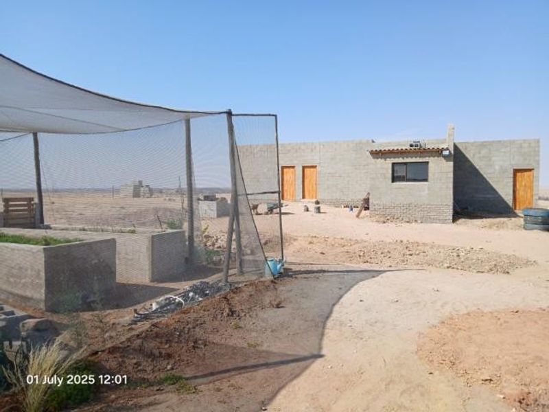 Rear view of a small holding property featuring unfinished concrete block structures, timber doors, and a shaded outdoor garden area.