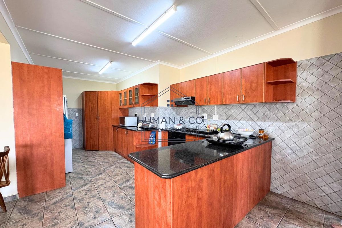 A functional kitchen featuring wood-finish cabinetry, granite countertops, a built-in hob, and an extractor fan, complemented by tiled flooring and backsplash.