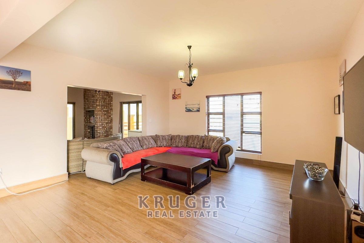 Spacious living room featuring wood-look tile flooring, large windows with blinds, and an open-plan layout leading to an adjacent area with a brick fireplace.