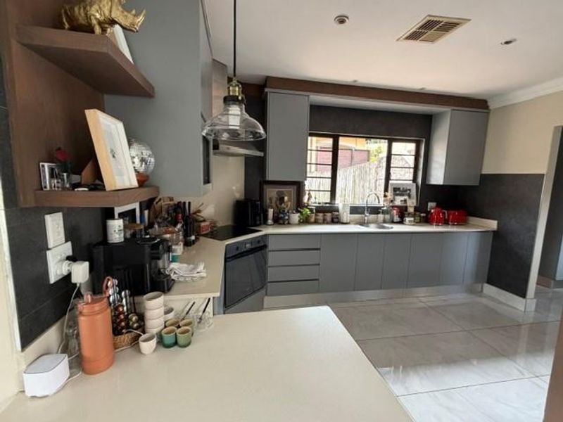 Modern kitchen featuring grey cabinetry, stone countertops, integrated oven, and sleek tiled flooring, offering a functional and contemporary cooking space.
