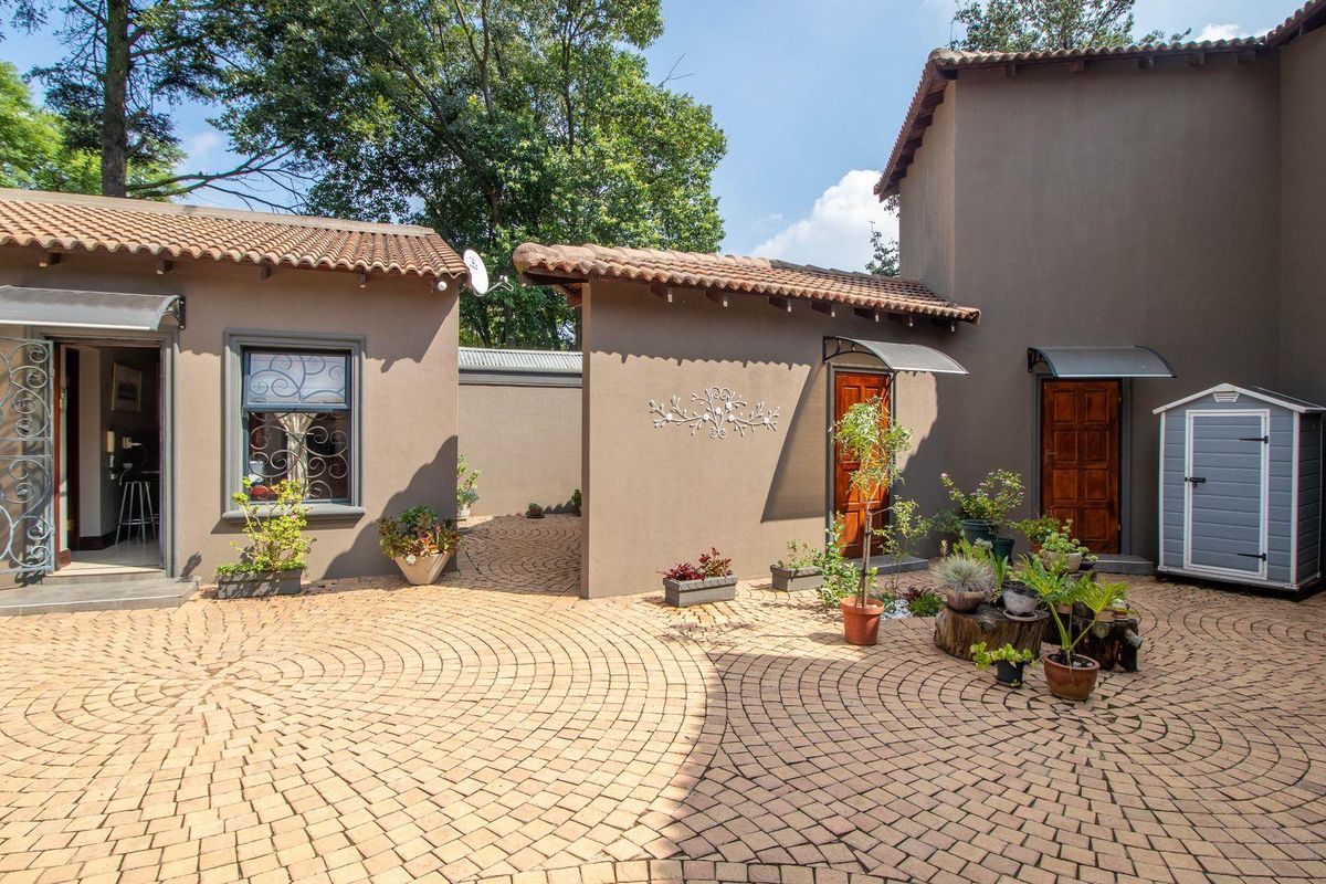 A paved courtyard area featuring multiple entry points to the home, terracotta roof tiles, and decorative metal security gates.