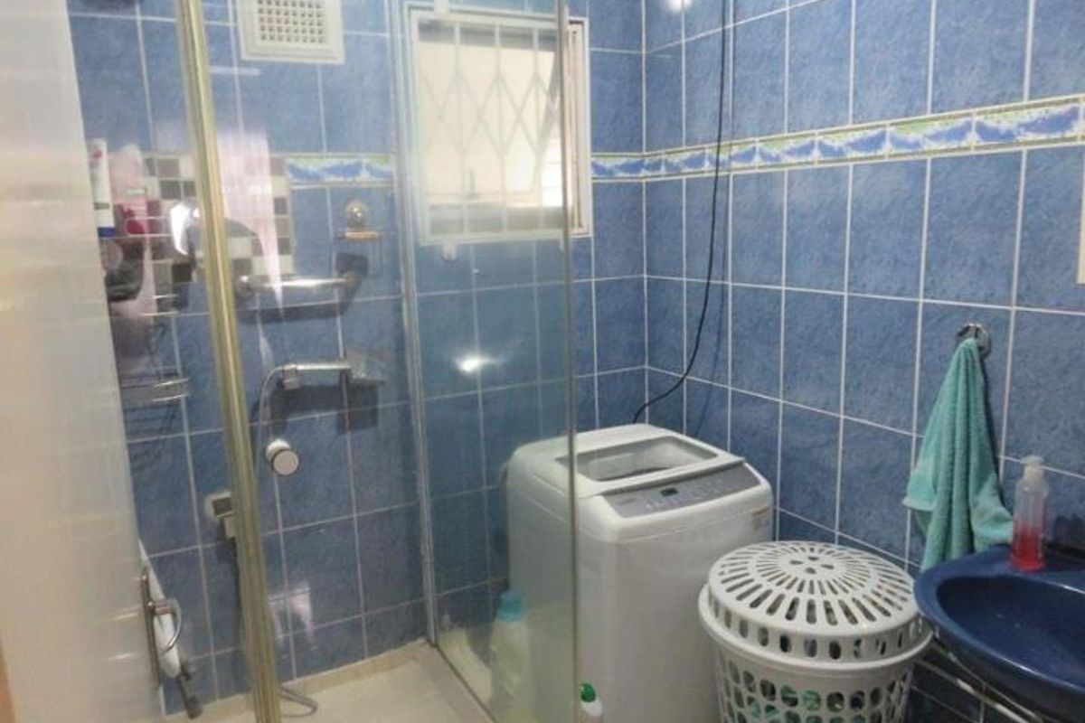 A compact bathroom featuring blue wall tiling, a glass shower enclosure, and a pedestal basin, with a window providing natural light.