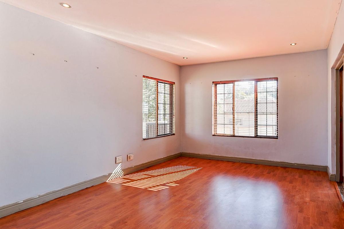 A vacant bedroom featuring laminate flooring, recessed downlights, and windows fitted with security bars and venetian blinds.