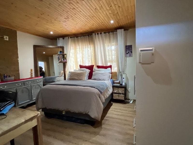 A bedroom featuring a warm timber-clad ceiling, laminate flooring, and a wall-mounted security alarm keypad.
