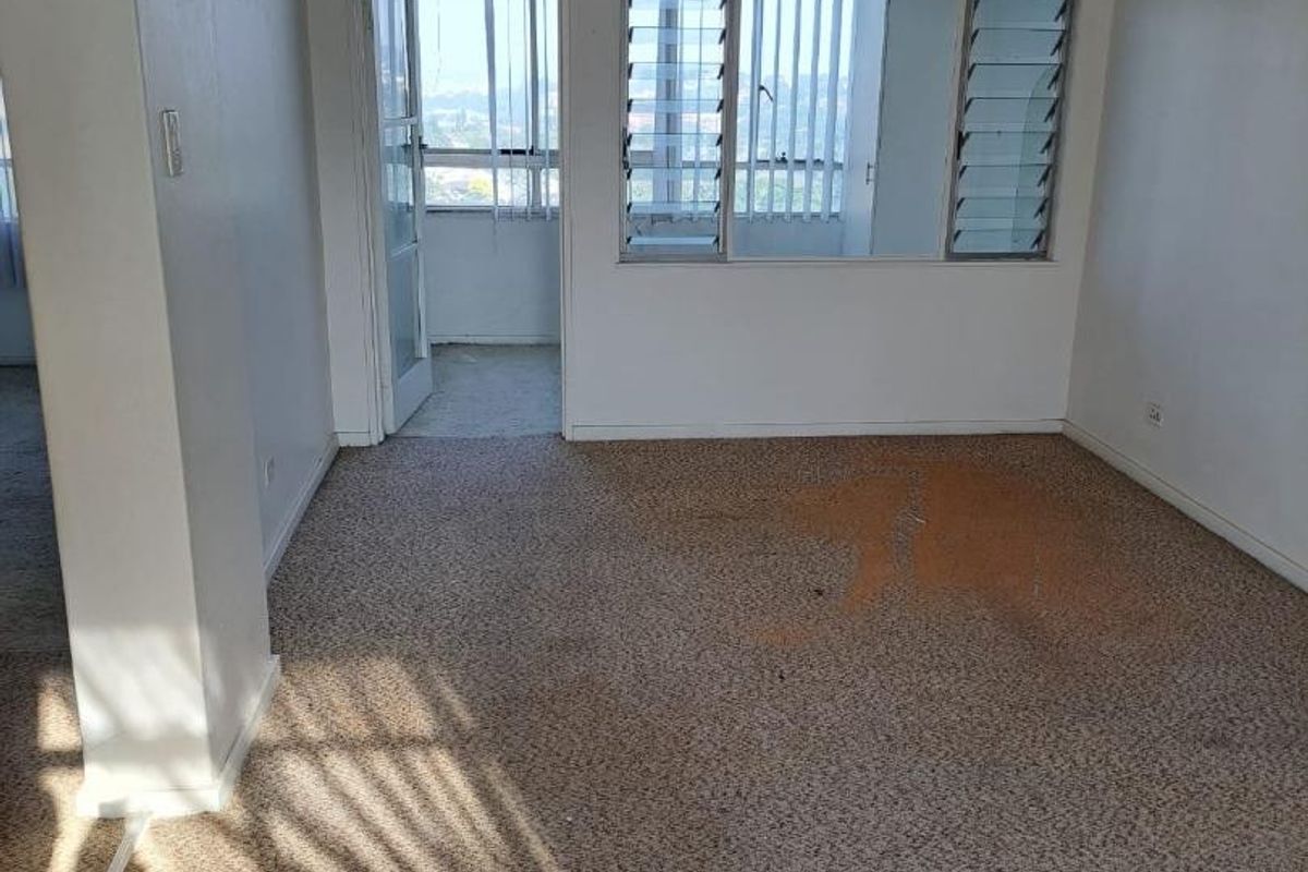 An empty living room featuring carpet flooring, a ceiling fan, and louver windows leading to an adjacent balcony area.