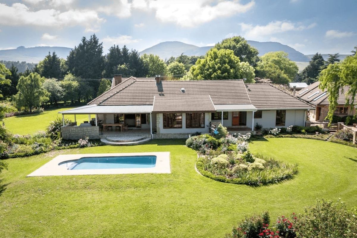 Aerial view of the guest house featuring a spacious rear garden, a swimming pool, and a covered patio area set against a scenic mountain backdrop.