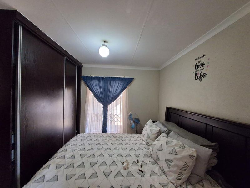 A functional bedroom featuring a large built-in sliding door wardrobe and a window fitted with a security gate.