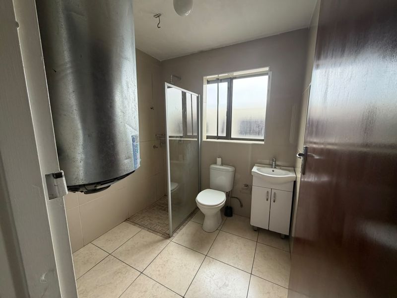 A functional bathroom featuring a shower enclosure, toilet, and vanity basin, with tiled finishes and an exposed water heater unit.