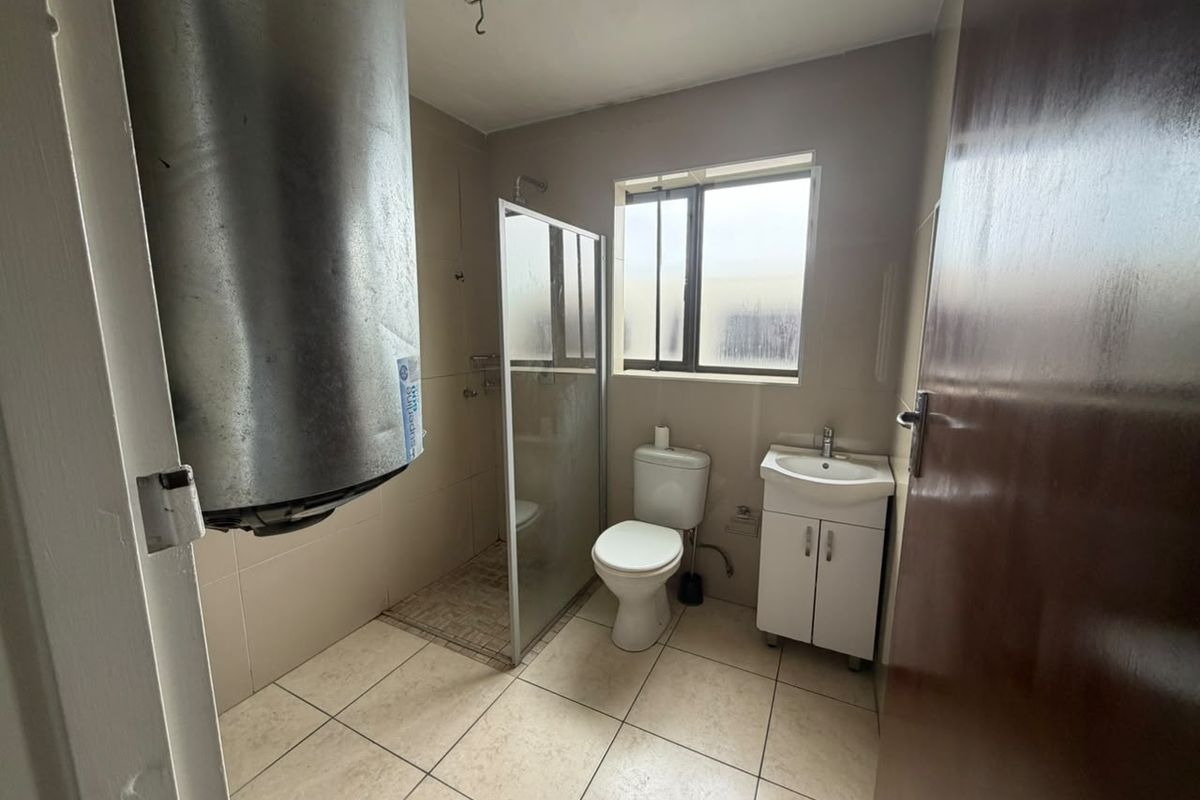A functional bathroom featuring a shower enclosure, toilet, and vanity basin, with tiled finishes and an exposed water heater unit.
