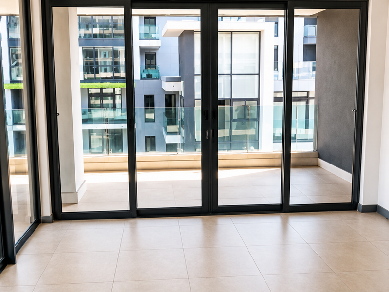 Bright, empty living area featuring large sliding glass doors that open onto a private balcony with modern tiled flooring and recessed lighting.