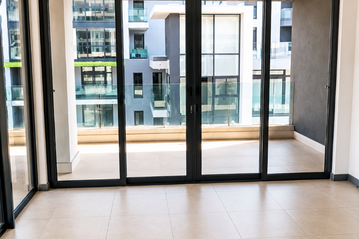 Bright, empty living area featuring large sliding glass doors that open onto a private balcony with modern tiled flooring and recessed lighting.