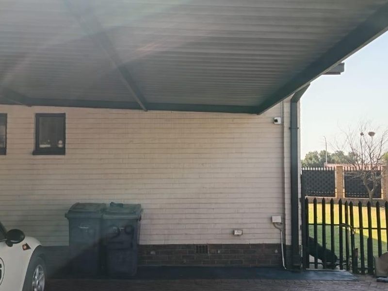A covered carport area featuring a brick facade, paved driveway, and secure perimeter fencing.