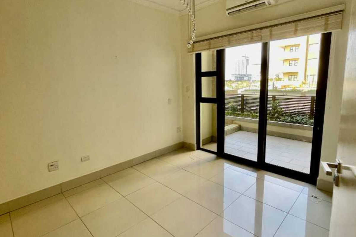 A bright, empty bedroom featuring tiled flooring, a wall-mounted air conditioning unit, and sliding glass doors that open onto a private balcony.
