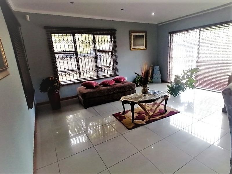 Spacious living room featuring polished tiled flooring, recessed downlighting, and large windows with security bars and venetian blinds, offering a bright and open atmosphere.