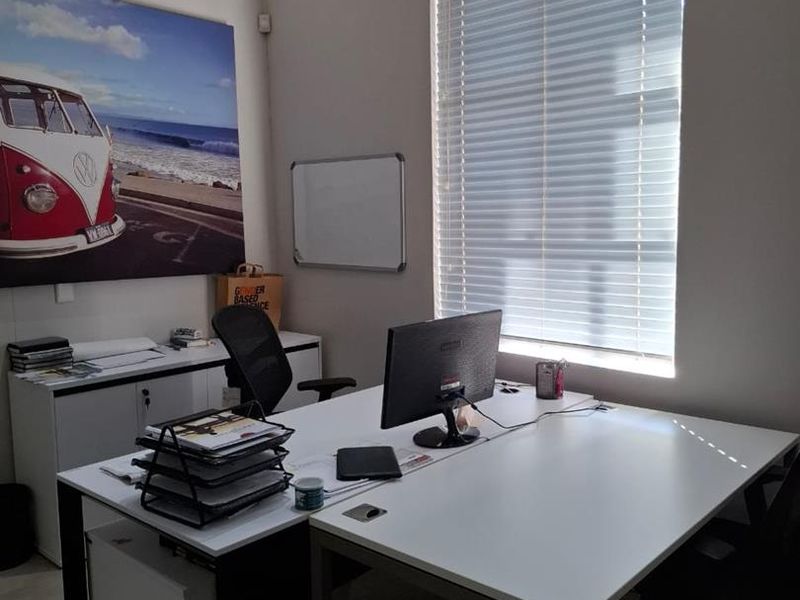 A functional office space featuring tiled flooring, a wall-mounted split-system air conditioner, and venetian blinds for light control.