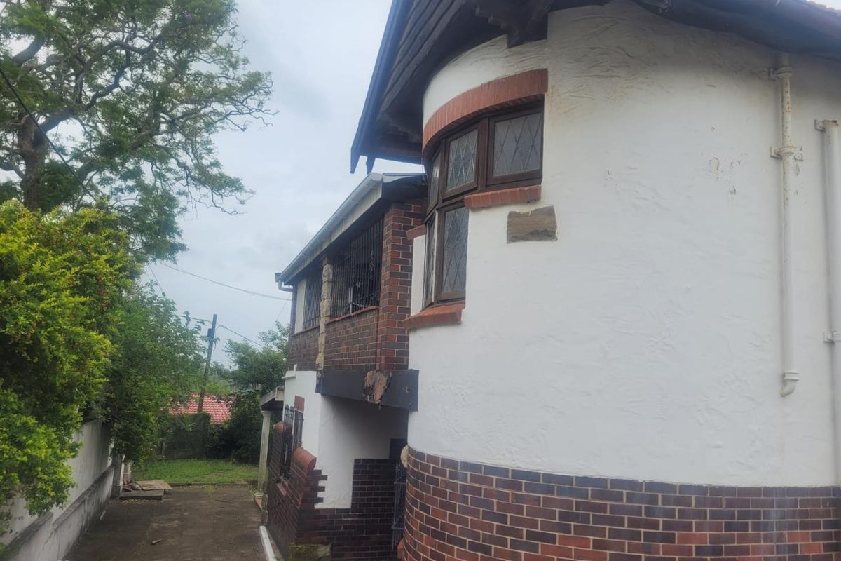 Side and rear view of the property featuring a distinctive curved wall design, brick facade, and leaded glass windows with visible exterior maintenance requirements.