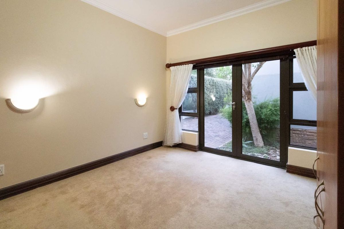 A bright, empty bedroom featuring neutral carpeting, crown molding, wall-mounted sconce lighting, and sliding glass doors providing direct access to the garden area.