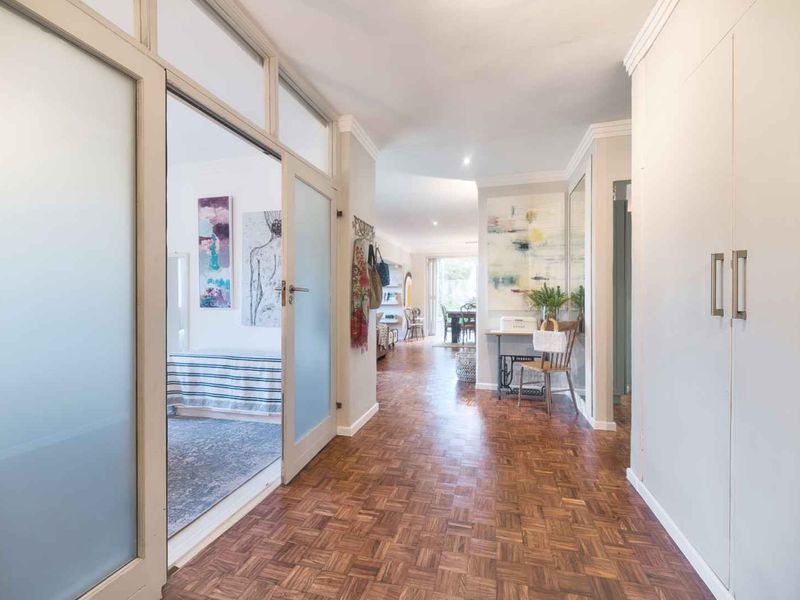 A bright, well-maintained hallway featuring classic parquet flooring, built-in storage cupboards, and elegant frosted glass panel doors leading to adjacent living spaces.