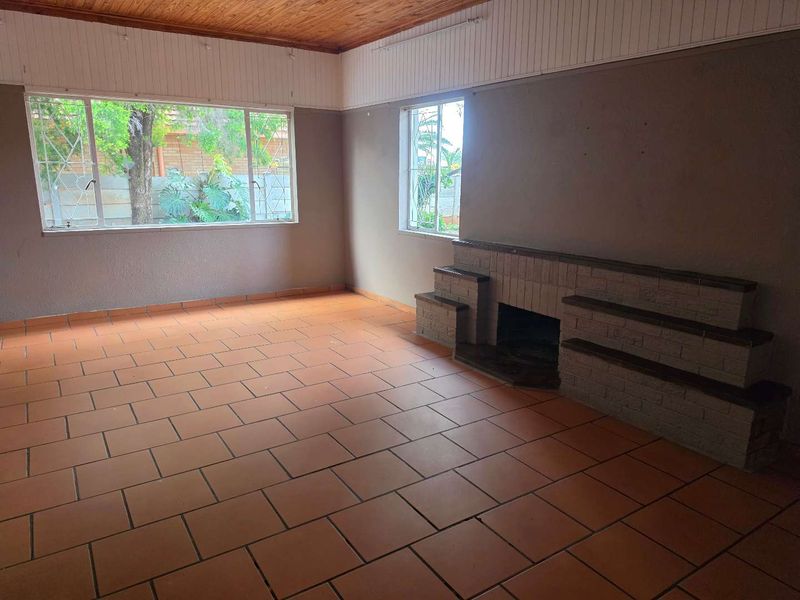 Spacious living room featuring terracotta tile flooring, a built-in brick fireplace, and a timber-paneled ceiling with large windows providing natural light.