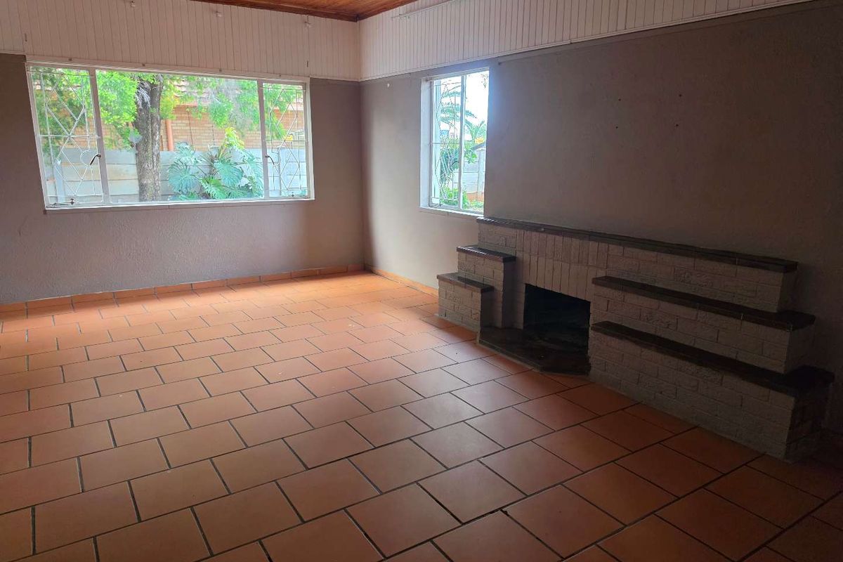 Spacious living room featuring terracotta tile flooring, a built-in brick fireplace, and a timber-paneled ceiling with large windows providing natural light.