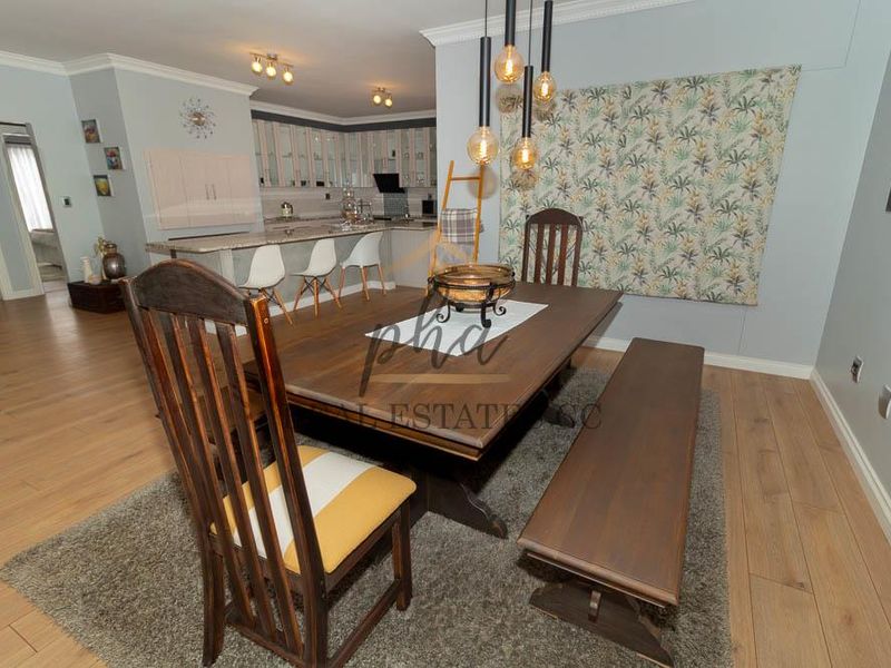 Open plan dining and kitchen area featuring laminate flooring, modern cabinetry, granite countertops, and stylish pendant lighting.