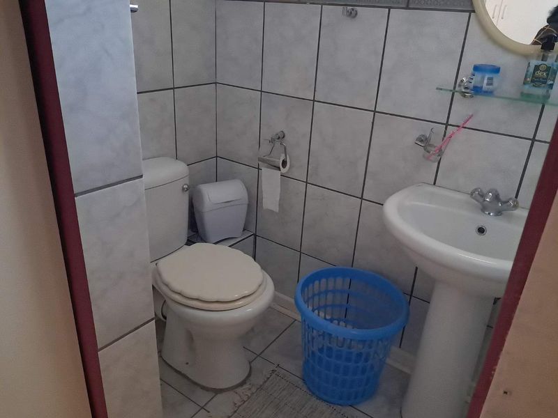 A functional bathroom featuring a pedestal basin, toilet, and neutral ceramic wall and floor tiling.
