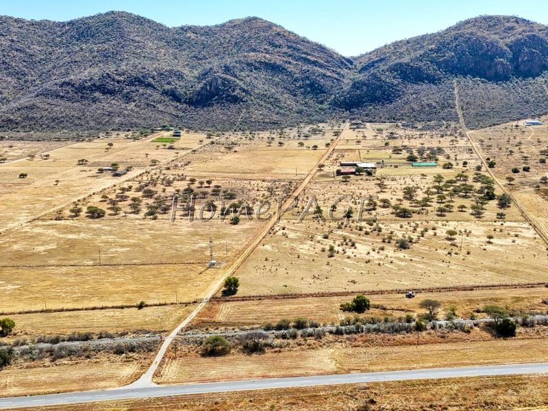 An aerial view of a large rural small holding property featuring expansive open land, mountain views, and established access roads.