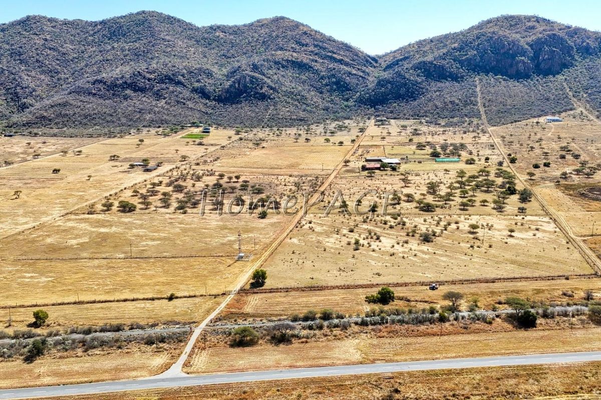 An aerial view of a large rural small holding property featuring expansive open land, mountain views, and established access roads.