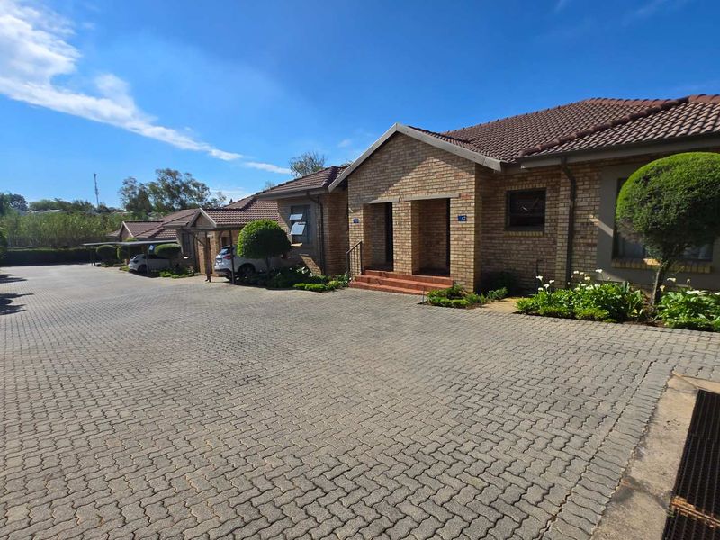 Front exterior view of a townhouse complex featuring face brick facades, tiled roofs, and a well-maintained paved driveway with landscaped garden areas.