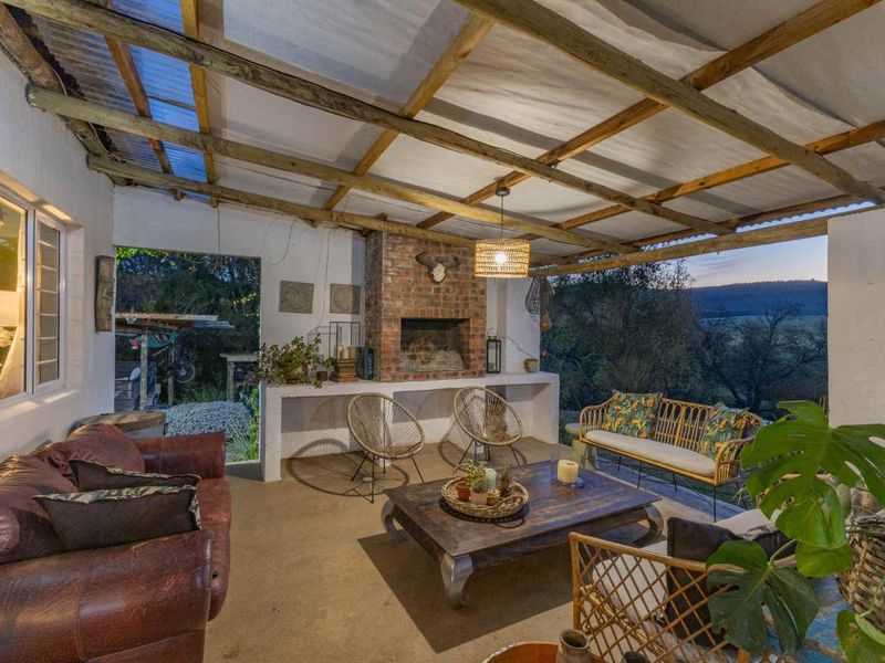 Covered outdoor patio featuring a rustic brick fireplace, concrete counter, and exposed timber beam ceiling, offering scenic views of the surrounding landscape.
