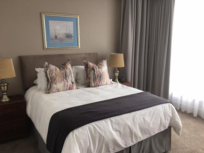A well-maintained bedroom featuring neutral wall tones, carpeted flooring, and floor-to-ceiling curtains providing natural light control.