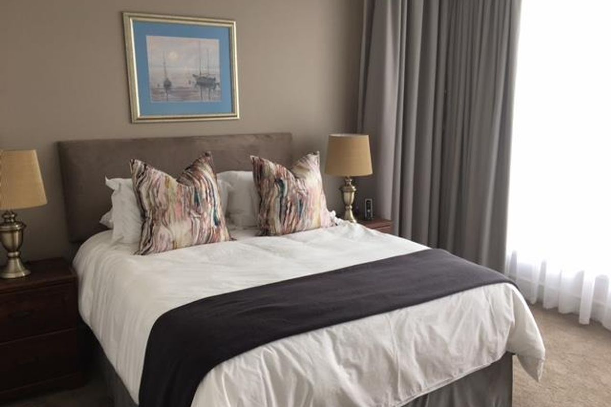 A well-maintained bedroom featuring neutral wall tones, carpeted flooring, and floor-to-ceiling curtains providing natural light control.