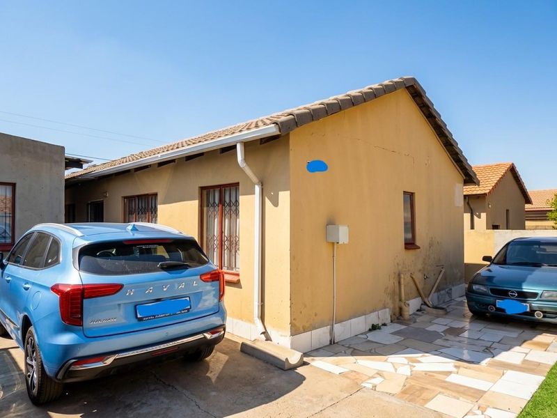 Rear exterior view of the property featuring a tiled roof, paved patio area, and security bars on the windows.