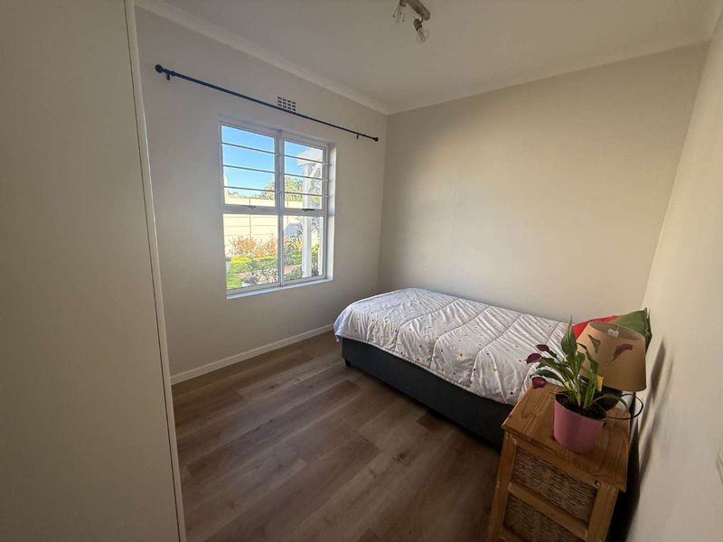 A bright bedroom featuring laminate flooring, a built-in wardrobe, and a window fitted with security bars.