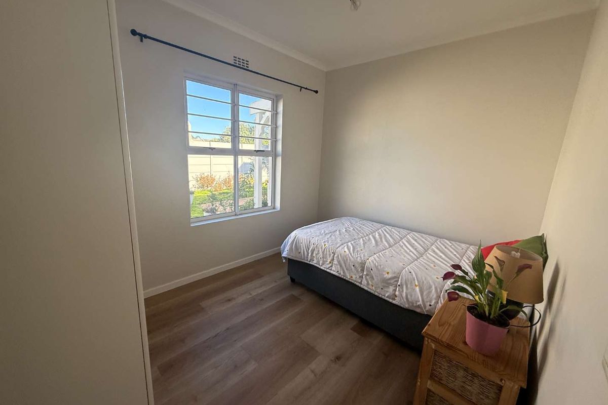 A bright bedroom featuring laminate flooring, a built-in wardrobe, and a window fitted with security bars.