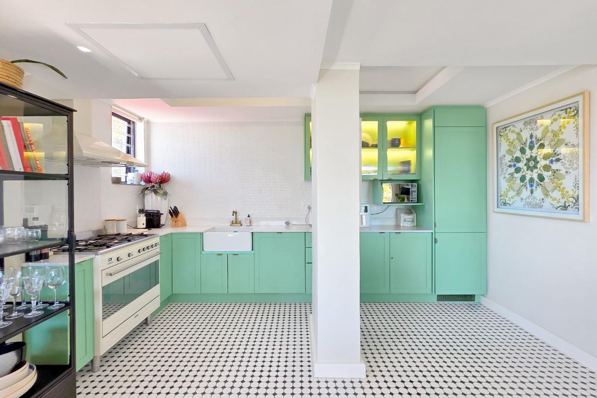 A bright, well-maintained kitchen featuring mint green cabinetry, a classic apron sink, gas stove, and stylish mosaic tile flooring.