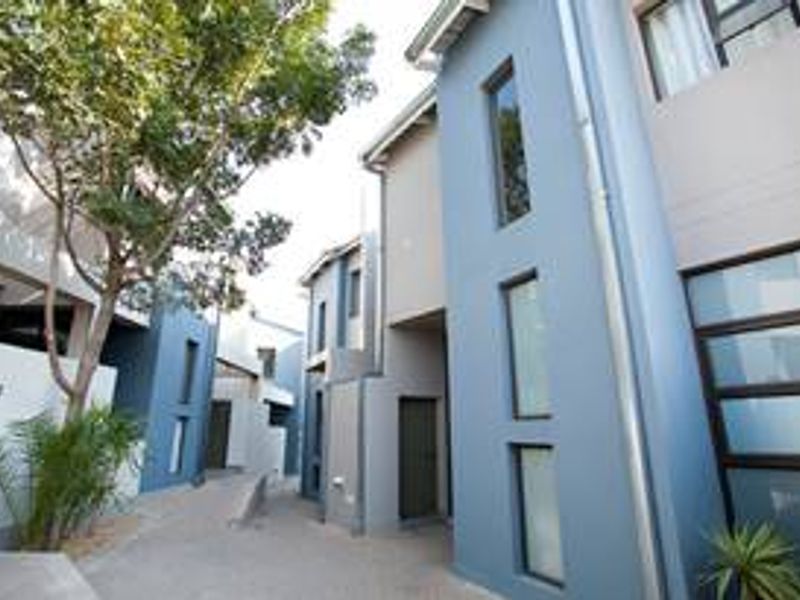 A modern townhouse exterior featuring a paved walkway, multi-story blue and grey facade, and vertical window design within a well-maintained residential complex.