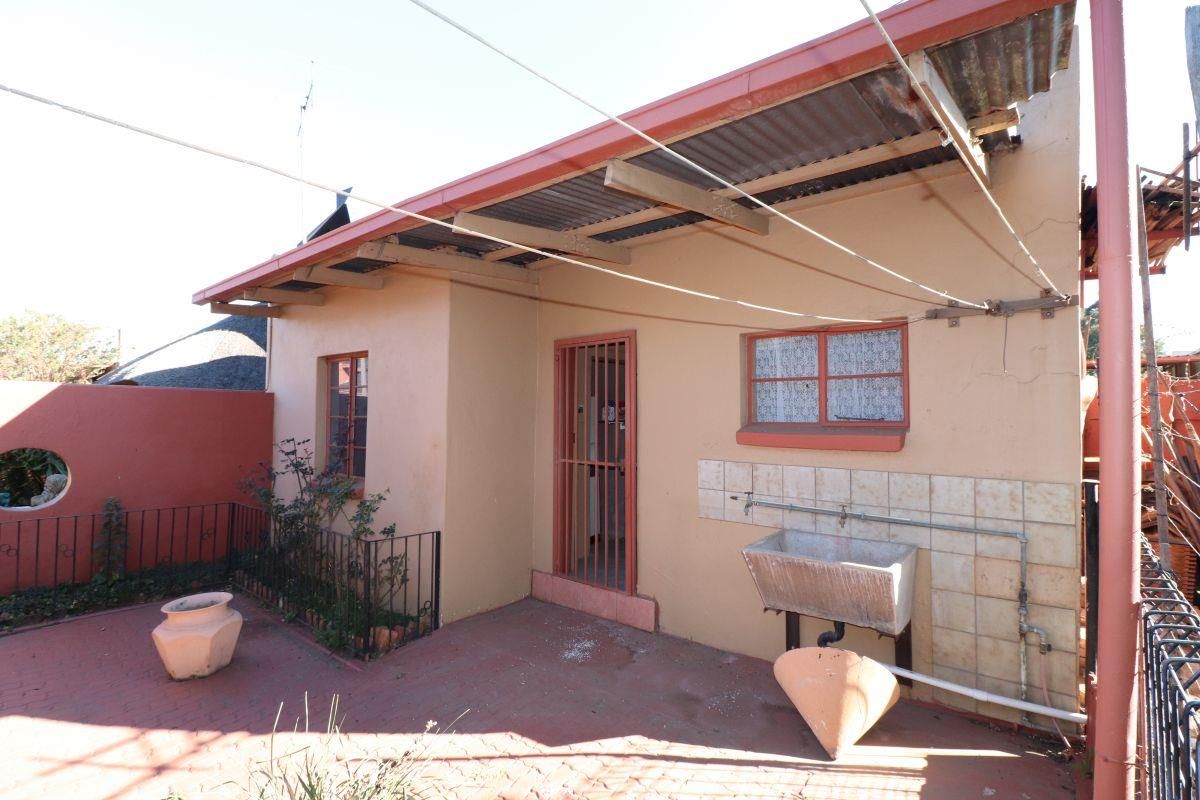 Rear exterior view featuring a paved patio area, a built-in concrete laundry trough, and a corrugated metal roof structure.