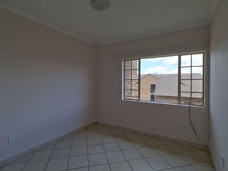 An empty bedroom featuring tiled flooring, a grid-pattern window, and neutral wall finishes, offering a blank canvas for personalization.