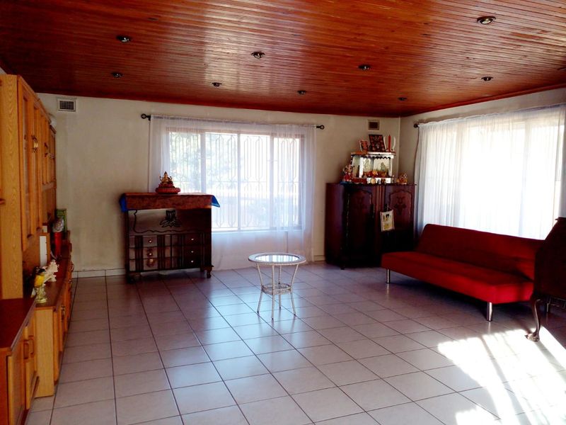 Spacious living room featuring ceramic floor tiles, a timber tongue and groove ceiling with recessed lighting, and large windows with security bars.