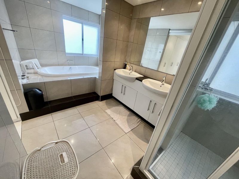 Modern bathroom featuring a built-in bathtub, double vanity with integrated sinks, large wall mirror, and a separate glass-enclosed shower with tiled finishes.